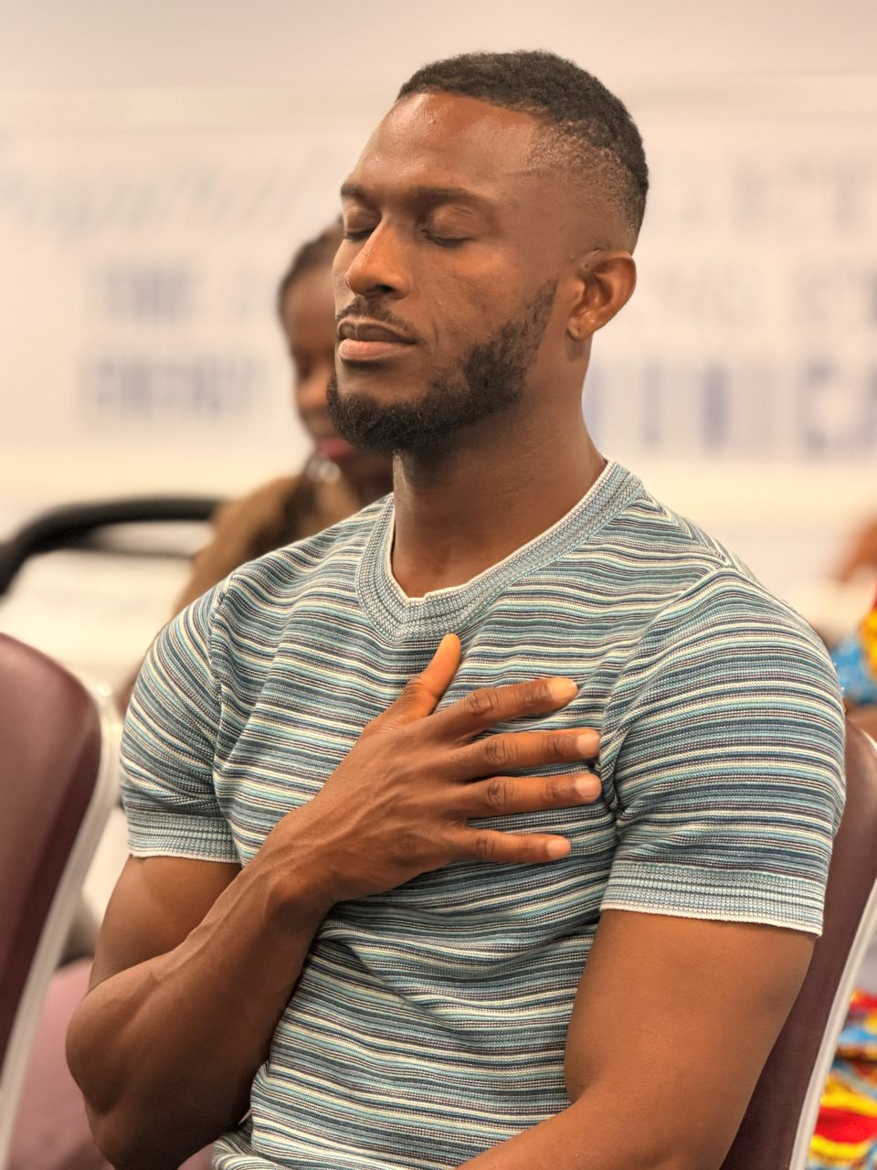 An attendee seated with eyes closed and a hand resting on his chest at Dwell 2026